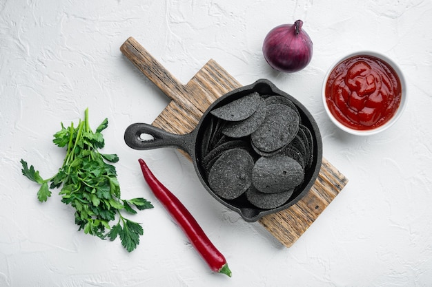 Croustilles de pommes de terre croustillantes noires, avec trempette sauce tomate crème sure, dans une poêle en fonte, sur une surface en pierre blanche, vue de dessus à plat