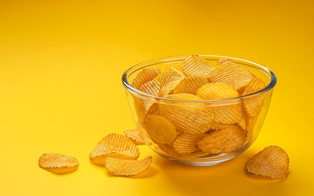 Croustilles striées dans un bol en verre isolé sur fond jaune