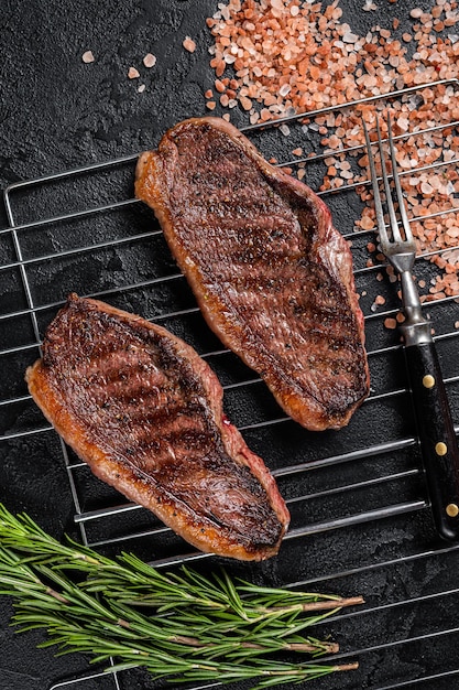 Croûte de chapeau grillé au barbecue ou steak de bœuf de surlonge, viande frite sur le gril. Fond noir. Vue de dessus.