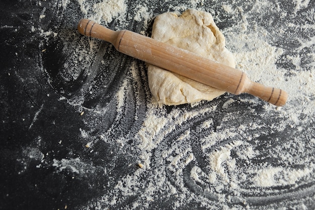 Croûte de pâte sur une table noire, concept de fabrication de pizza, rouleau à pâtisserie en bois.