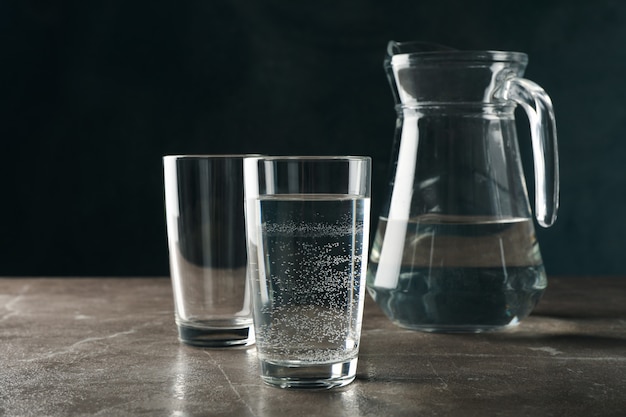 Cruche avec de l'eau et des verres sur table grise, espace pour le texte