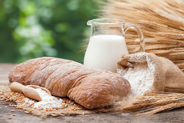 Cruche de pain frais de sac de lait avec farine et gerbe de blé sur table en bois