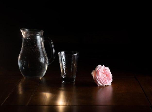 Cruche en verre avec de l'eau sur un fond sombre avec une rose