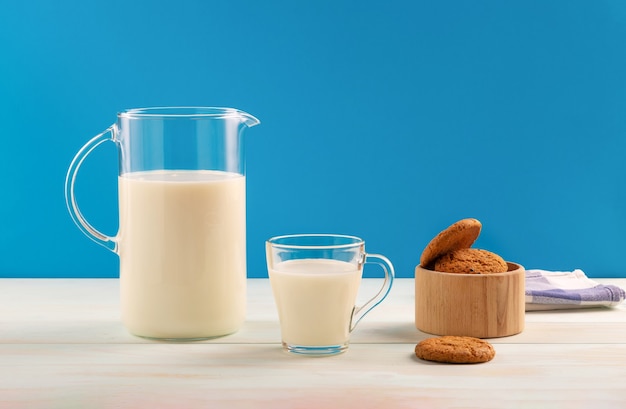 Une cruche et un verre de lait avec des cookies sur une table en bois sur bleu