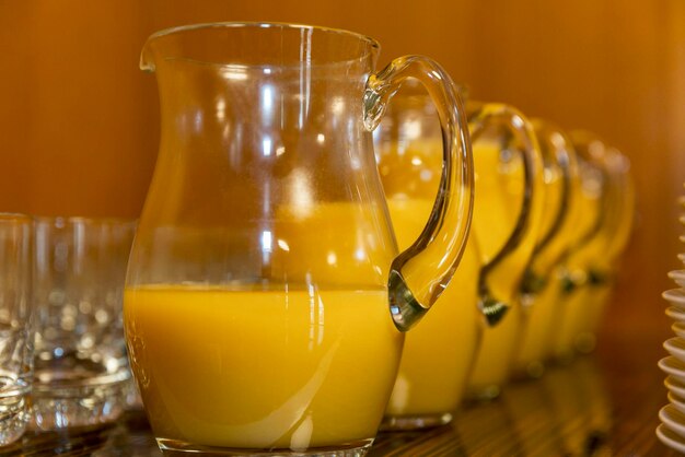 Cruches de jus d'orange rangées de verres vides et piles d'assiettes sur une table de buffet Fêtes et célébrations