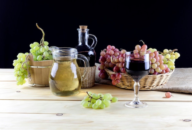 Cruches de raisins mûrs verts et roses et vin dans le verre sur la table sur un gros plan de fond noir