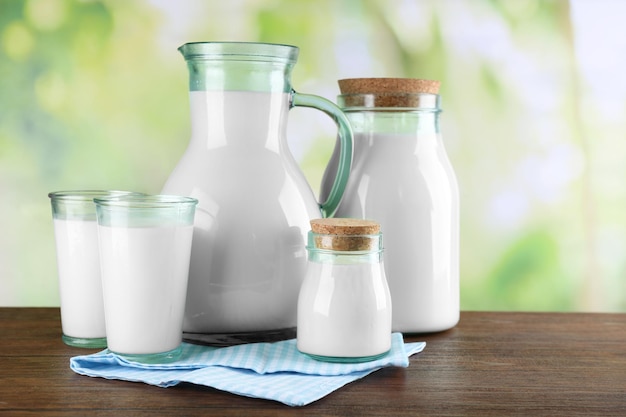 Des cruches et des verres de lait sur une table en bois sur un fond naturel