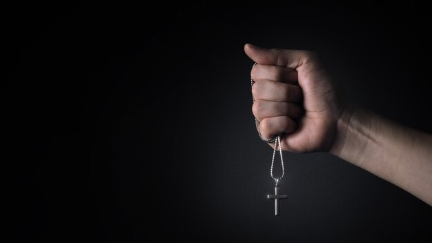 Crucifix en argent ou pendentif en croix et collier sur le corps ou la main tourné en studio fond de couleur noire