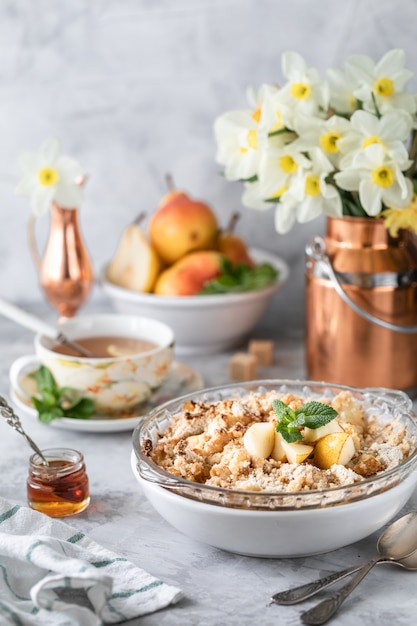 Crumble de poire au four avec des poires et du miel dans un plat blanc sur la table avec des ustensiles en cuivre et des fleurs