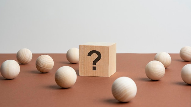 Cube en bois avec un point d'interrogation entouré de boules en bois sur un fond de table marron