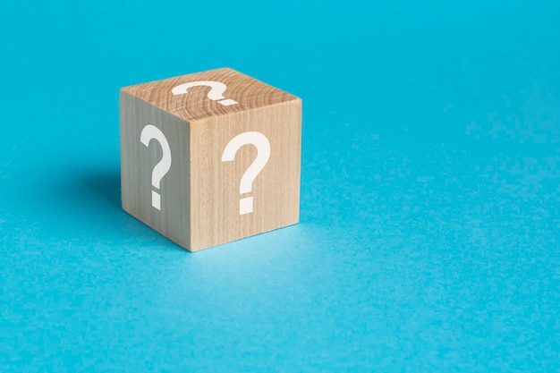 Cube jouet en bois avec des points d'interrogation blancs vu grand angle sur un fond bleu