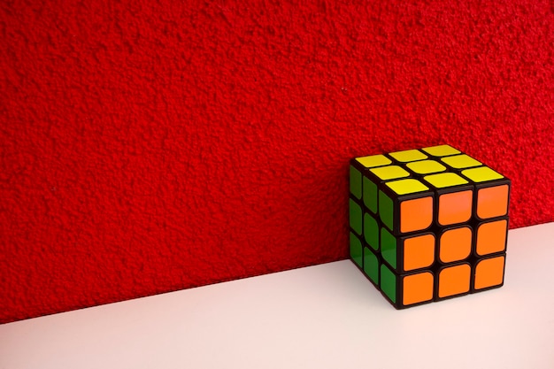 Cube de vitesse de puzzle résolu sur une étagère en bois blanc près d'un mur de couleur rouge cube rubiks coloré avec copie ...