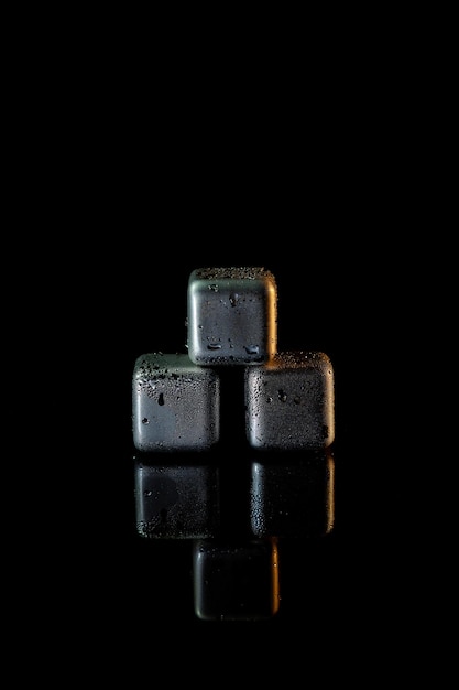 Cubes en acier inoxydable simulant la glace pour refroidir les boissons sur une surface noire avec un reflet