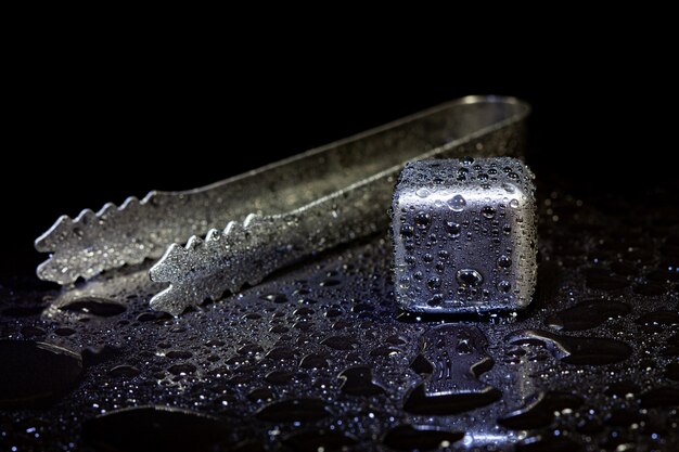 Cubes en acier inoxydable simulant de la glace pour refroidir les boissons sur une surface noire avec un reflet.