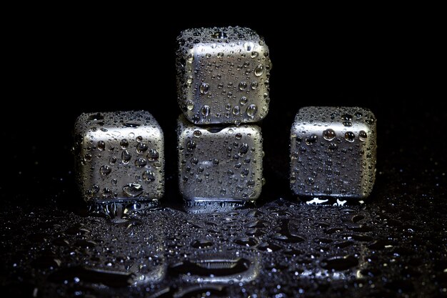 Cubes en acier inoxydable simulant de la glace pour refroidir des boissons sur une surface noire avec un reflet.