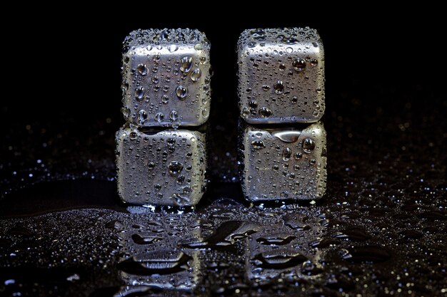 Cubes en acier inoxydable simulant de la glace pour refroidir des boissons sur une surface noire avec un reflet.