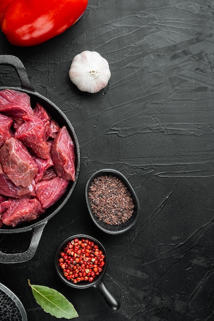 Cubes de boeuf cru frais sertis de poivron doux, dans une poêle à frire en fonte, sur fond de pierre noire, vue de dessus à plat, avec espace de copie pour le texte