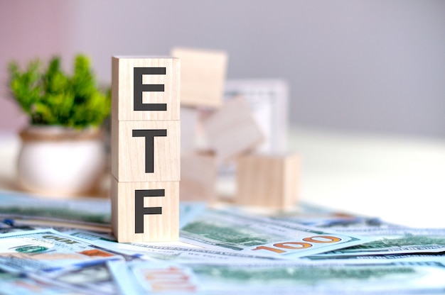 Cubes en bois avec les lettres ETF disposées en pyramide verticale sur les billets, plante verte dans un pot de fleurs sur l'arrière-plan. ETF - abréviation de Exchange-Traded Fund, concept d'entreprise.