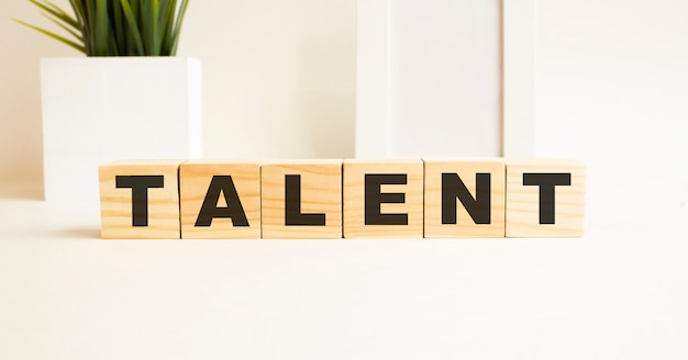 Cubes en bois avec des lettres sur un tableau blanc. Le mot est TALENT. Fond blanc avec cadre photo, plante d'intérieur.