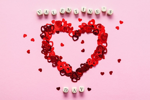 Cubes en bois avec les mots Saint Valentin et coeur fait de confettis en forme de coeur sur fond rose