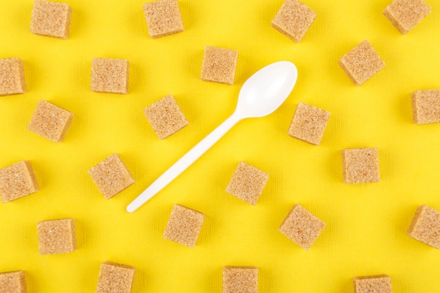 Cubes de cassonade et cuillère sur fond de papier jaune