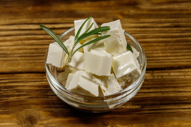 Cubes de fromage feta au romarin dans un bol en verre sur une table en bois