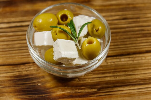 Cubes de fromage feta aux olives vertes et romarin dans un bol en verre sur une table en bois