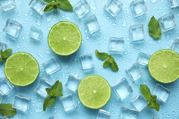 Cubes de glace à la menthe et citrons verts coupés sur fond turquoise à plat Ingrédients pour boisson rafraîchissante