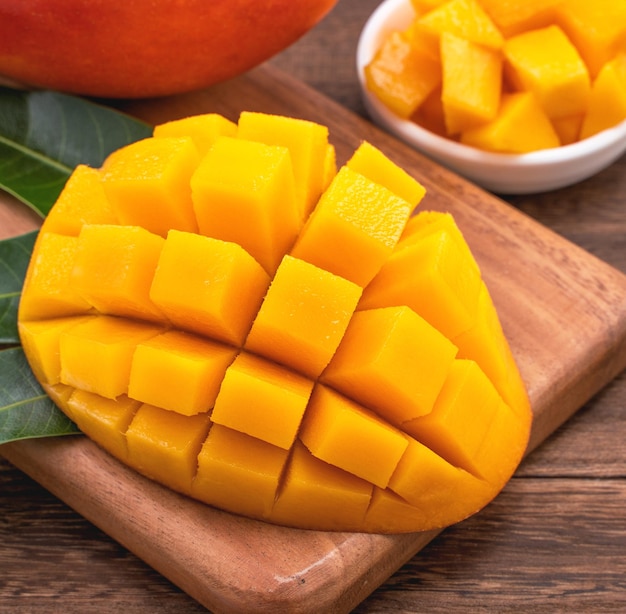 Cubes de mangue fraîche hachée sur planche à découper en bois et fond de bois rustique Concept de fruits d'été tropicaux gros plan macro copie espace