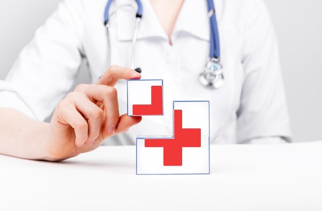 Cubes de premiers secours avec croix rouge dans les mains du médecin Soins médicaux urgents Femme en blouse de laboratoire avec stéthoscope assis à table