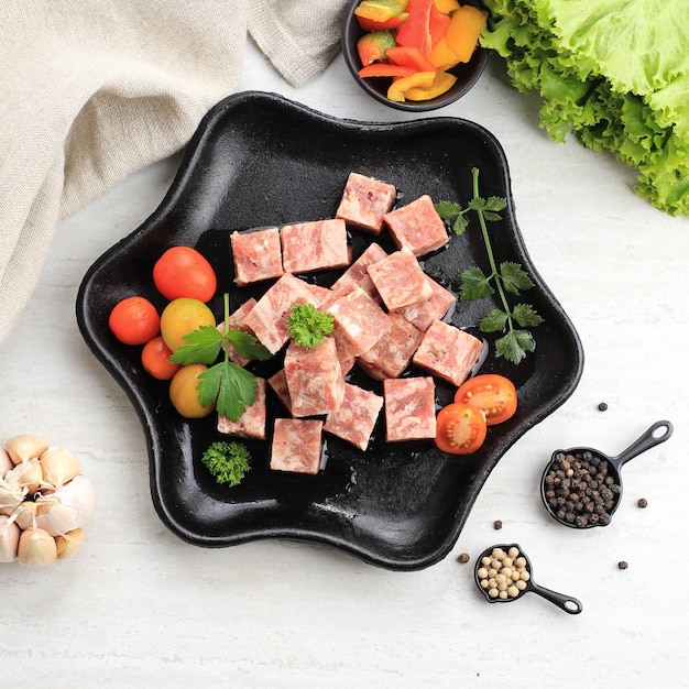 Cubes de Saikoro Wagyu surgelés crus ou steak de boeuf en dés sur une assiette de steak noir avec épices et légumes