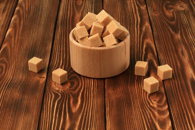 Cubes de sucre blanc et brun, bol en bois sur table en bois. Copiez l'espace.