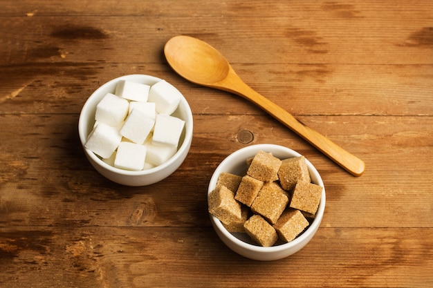 Cubes de sucre blanc et brun dans des bols en céramique blanche sur une table en bois