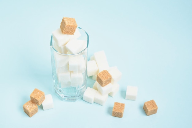 Cubes de sucre blanc et brun dans un verre et sur un espace de copie de fond bleu clair et beige, sucre dans les boissons et concept alimentaire