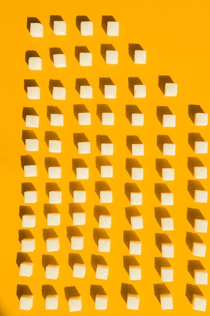 Cubes de sucre blanc disposés en lignes diagonales sur fond jaune