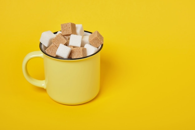 Cubes de sucre brun et blanc de canne dans une tasse jaune sur fond jaune copy space