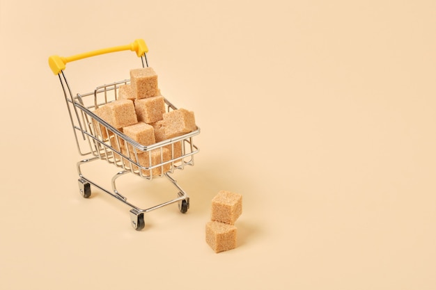 Cubes de sucre brun dans un caddie miniature sur une surface beige