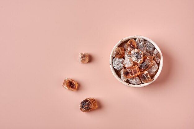 Cubes de sucre de canne caramélisé brun dans un bol sur fond en poudre rose vue de dessus copie espace