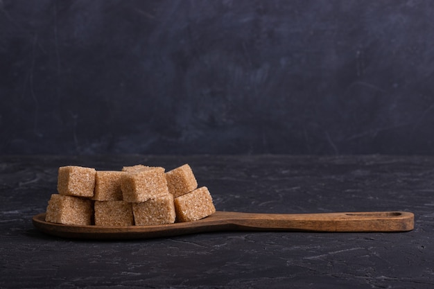 Cubes de sucre de canne dans une cuillère en bois sur un fond sombre