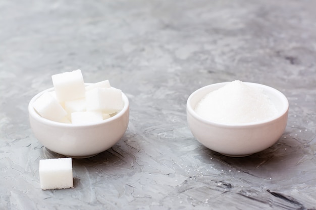 Cubes de sucre et sucre granulé dans des bols blancs sur une table