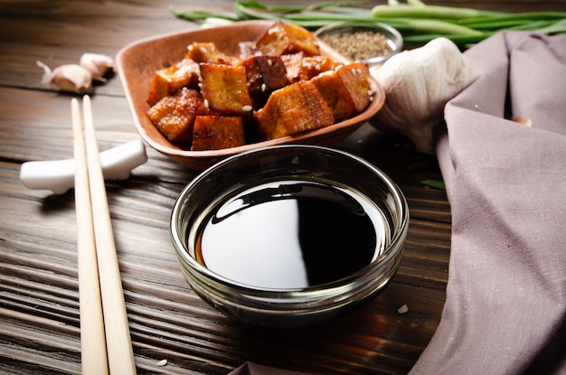 Cubes de tofu sautés croustillants à la ciboulette dans un plat en argile sur une table de cuisine en bois avec serviette