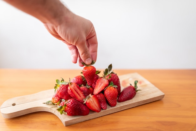 Cueillette à la main une fraise sur une planche à découper en bois.