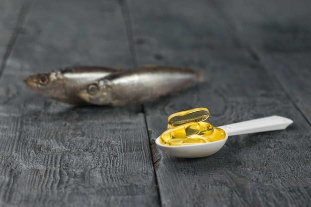 Une cuillère blanche avec des capsules d'huile de poisson sur le fond de deux poissons