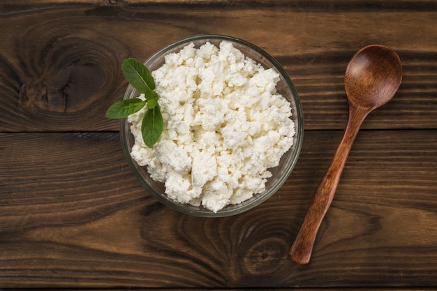 Une cuillère en bois et une assiette en verre avec du fromage cottage sur une table en bois