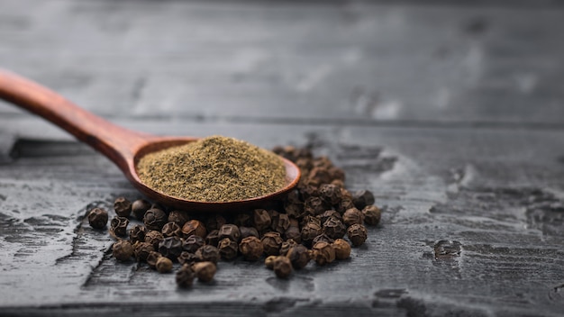 Une cuillère en bois avec du poivre noir moulu sur un tas de poivre entier sur une table en bois.