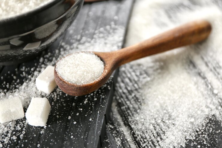 Photo cuillère en bois avec du sucre cristallisé blanc sur fond de bois noir