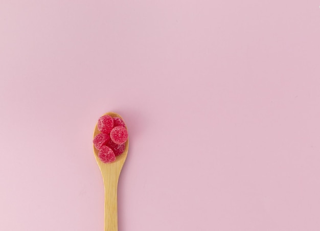 Cuillère en bois avec des fèves à la gelée rouges sur fond rose vue d'en haut