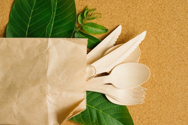 une cuillère en bois, une fourchette et un couteau sont attachés avec de la ficelle et sont dans un sac kraft.