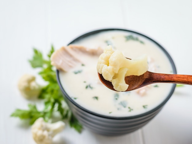 Cuillère en bois avec inflorescence de chou-fleur au-dessus d&#39;un bol avec soupe au chou et au poulet.