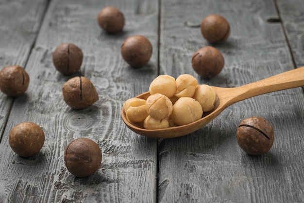 Une cuillère en bois avec des noix de macadamia pelées et des noix non pelées éparpillées. Superaliments.